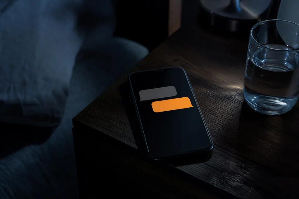 A phone on a dark nightstand lighting up with a new message